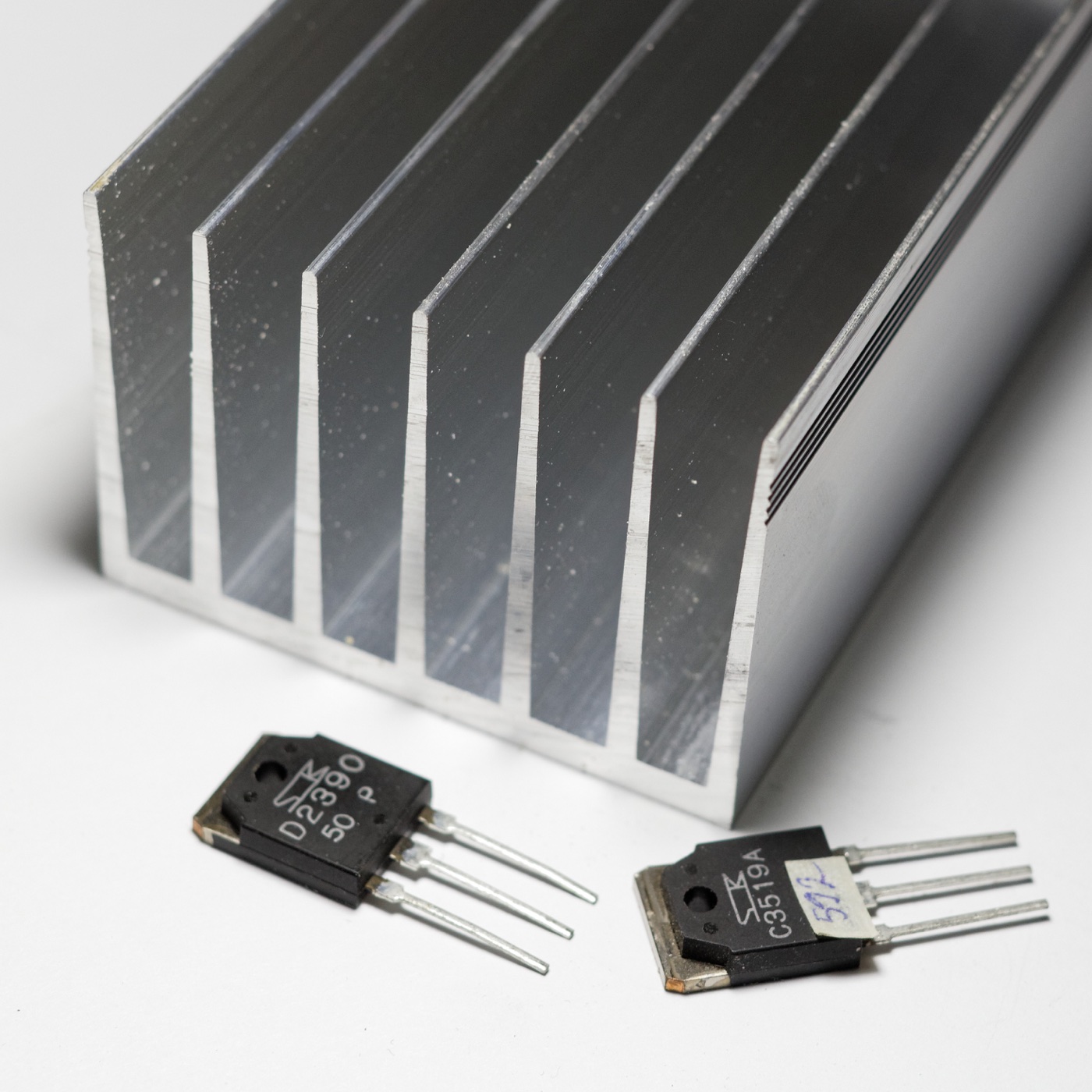 Aluminum heatsink with deep fins photographed beside two power transistors